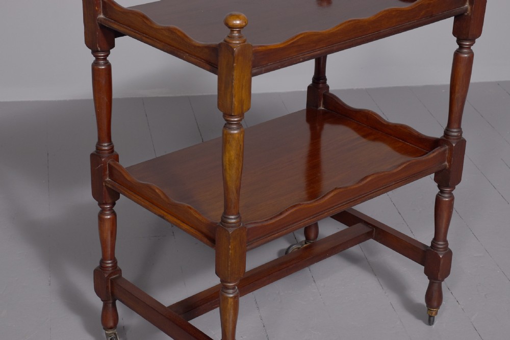 A two-tier mahogany wooden trolley featuring turned upright posts, brass castors, decorative inlay, and scalloped gallery borders. View III