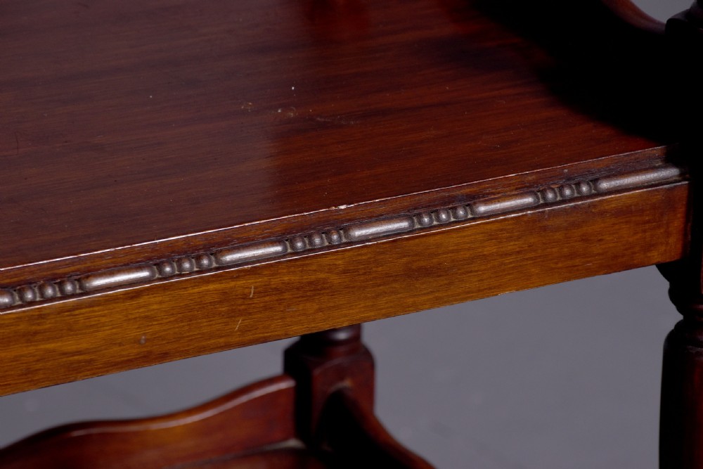 A two-tier mahogany wooden trolley featuring turned upright posts, brass castors, decorative inlay, and scalloped gallery borders. View VII