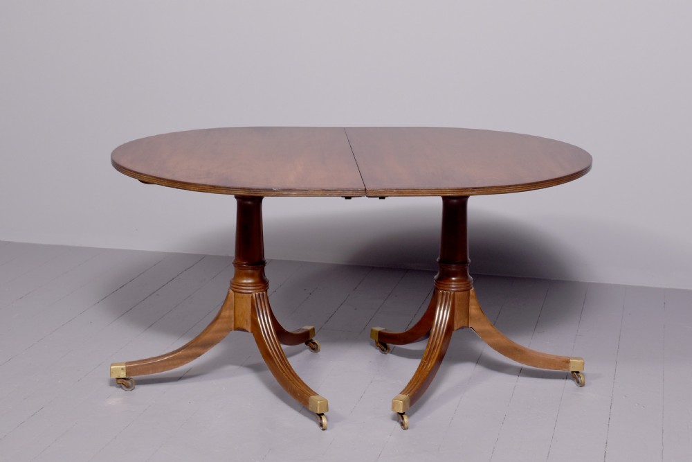 A mahogany twin pillar dining table featuring reeded splayed legs with brass castors and a polished wood finish.