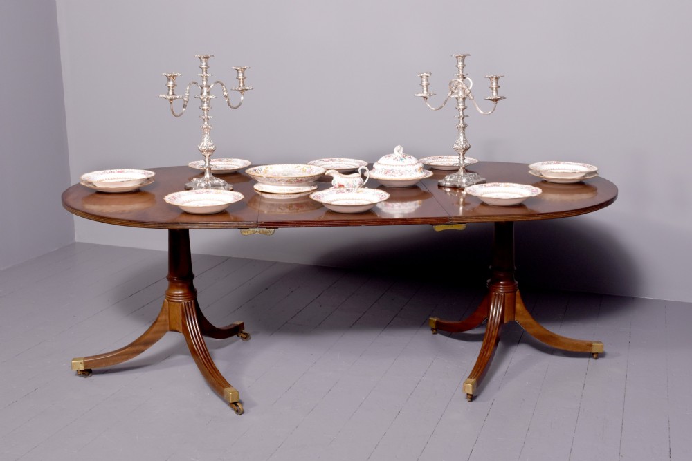 A mahogany twin pillar dining table featuring reeded splayed legs with brass castors and a polished wood finish. View IV