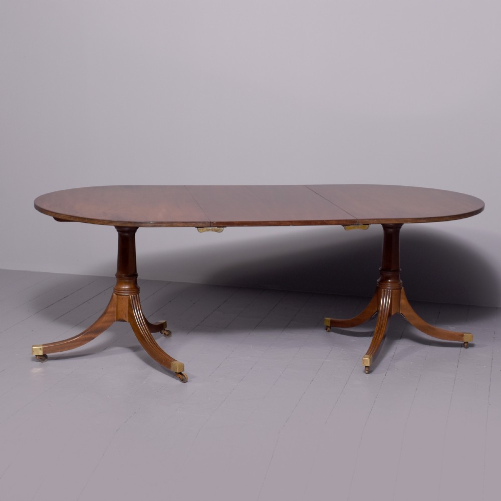 A mahogany twin pillar dining table featuring reeded splayed legs with brass castors and a polished wood finish. View V