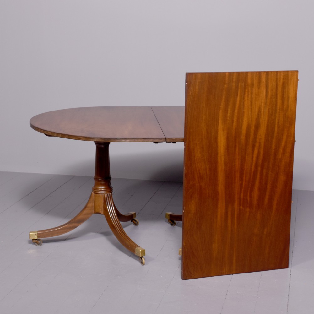 A mahogany twin pillar dining table featuring reeded splayed legs with brass castors and a polished wood finish. View VI