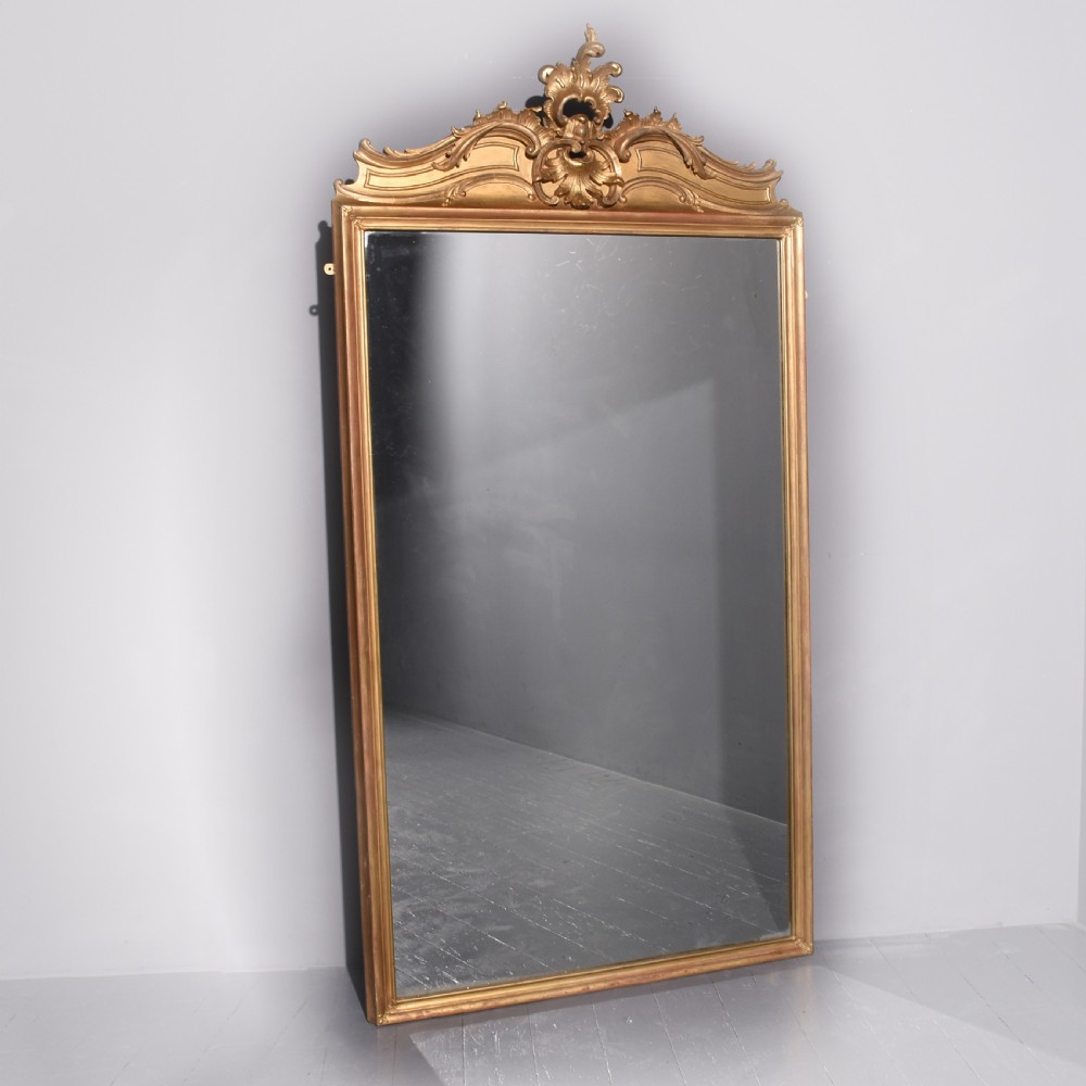 A large Victorian giltwood overmantle mirror featuring a curved top frame surmounted by a carved rococo cresting motif.