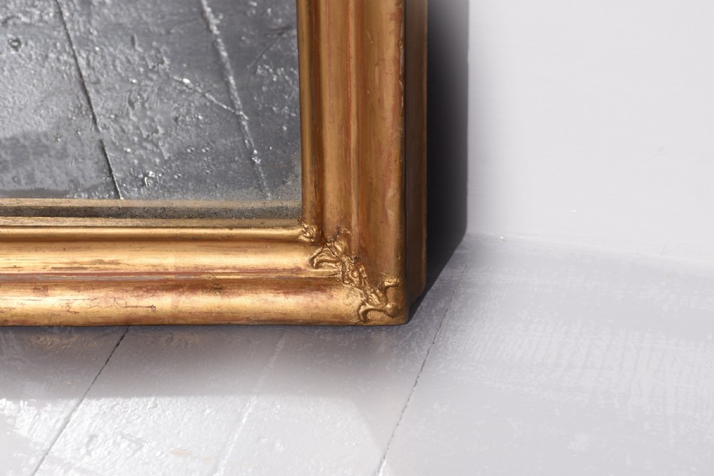 A large Victorian giltwood overmantle mirror featuring a curved top frame surmounted by a carved rococo cresting motif. View III