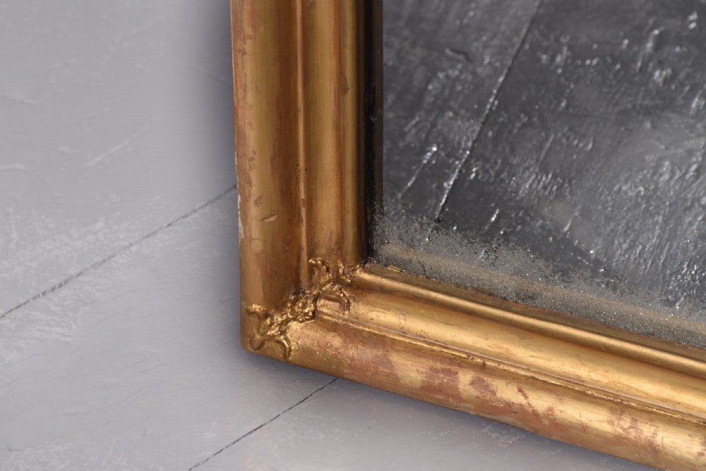 A large Victorian giltwood overmantle mirror featuring a curved top frame surmounted by a carved rococo cresting motif. View IV