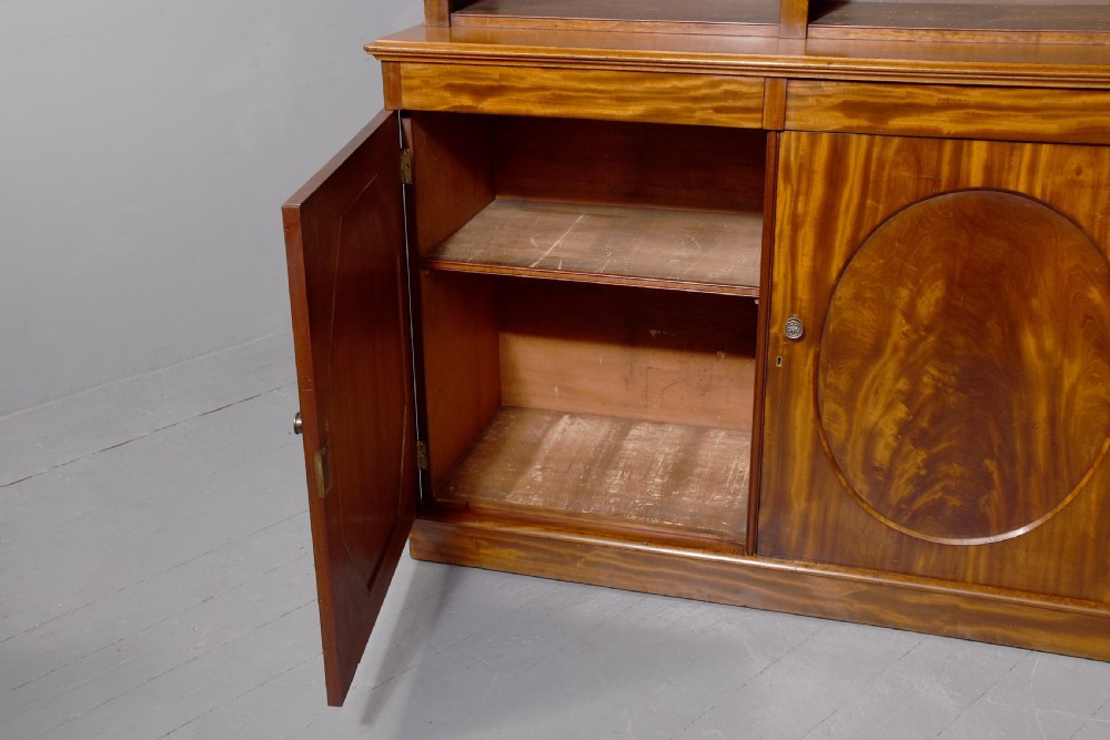A large mid-Victorian mahogany bookcase featuring a three-bay open upper section with adjustable shelves set above a three-door cupboard base with oval veneered panels. View III