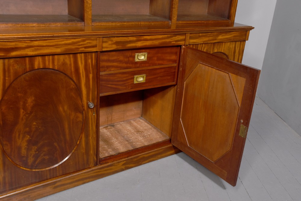 A large mid-Victorian mahogany bookcase featuring a three-bay open upper section with adjustable shelves set above a three-door cupboard base with oval veneered panels. View V
