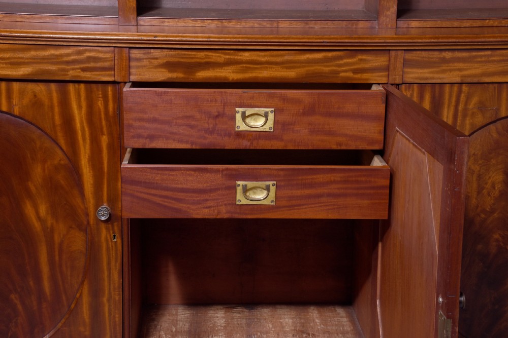A large mid-Victorian mahogany bookcase featuring a three-bay open upper section with adjustable shelves set above a three-door cupboard base with oval veneered panels. View VII