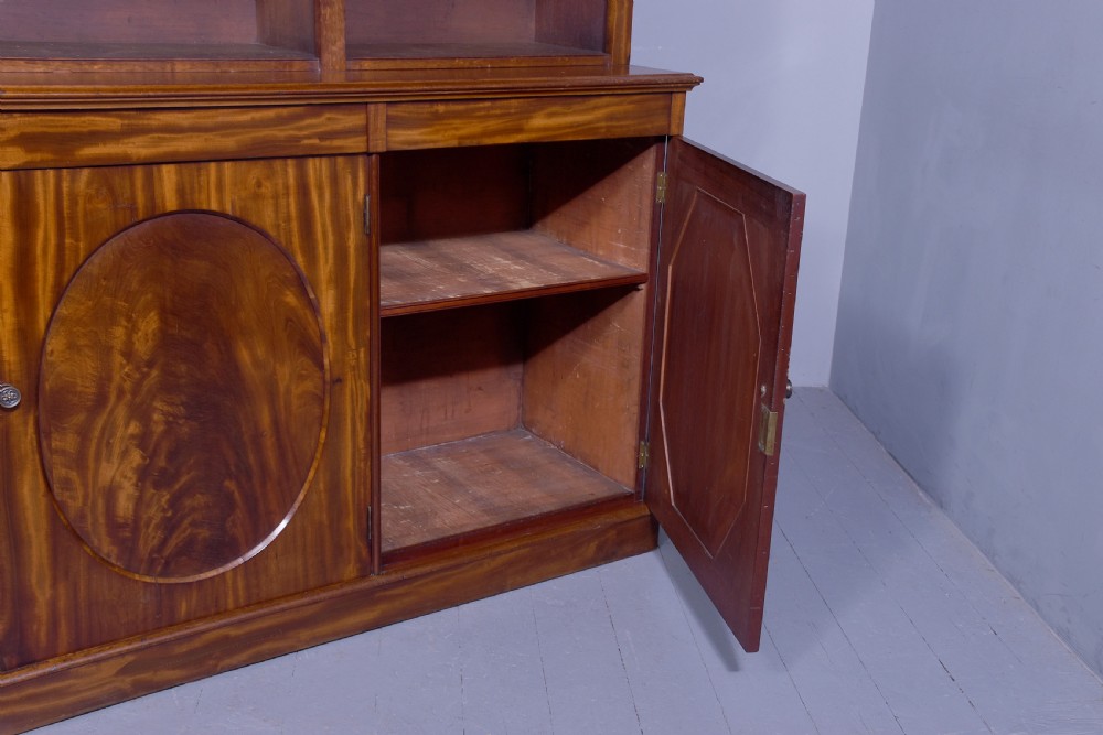 A large mid-Victorian mahogany bookcase featuring a three-bay open upper section with adjustable shelves set above a three-door cupboard base with oval veneered panels. View IX