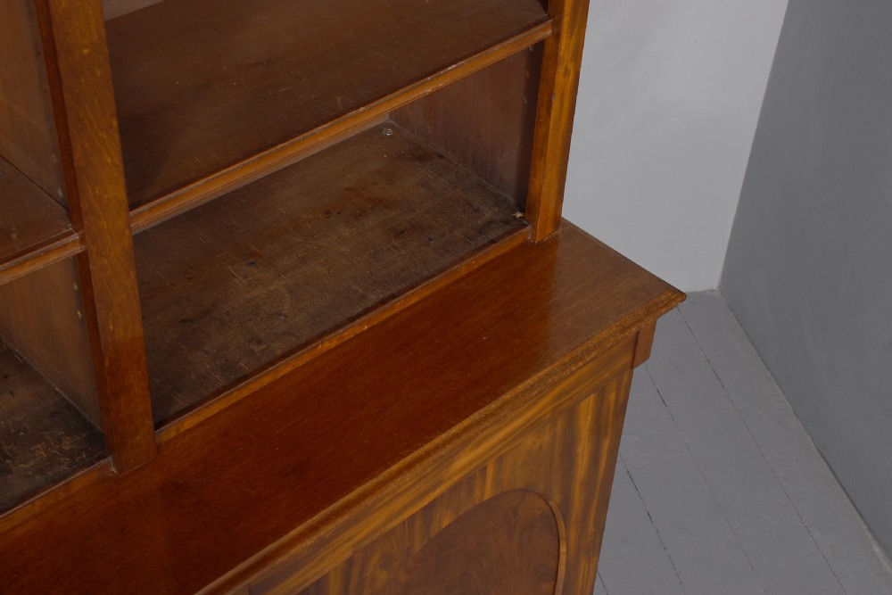 A large mid-Victorian mahogany bookcase featuring a three-bay open upper section with adjustable shelves set above a three-door cupboard base with oval veneered panels. View XII