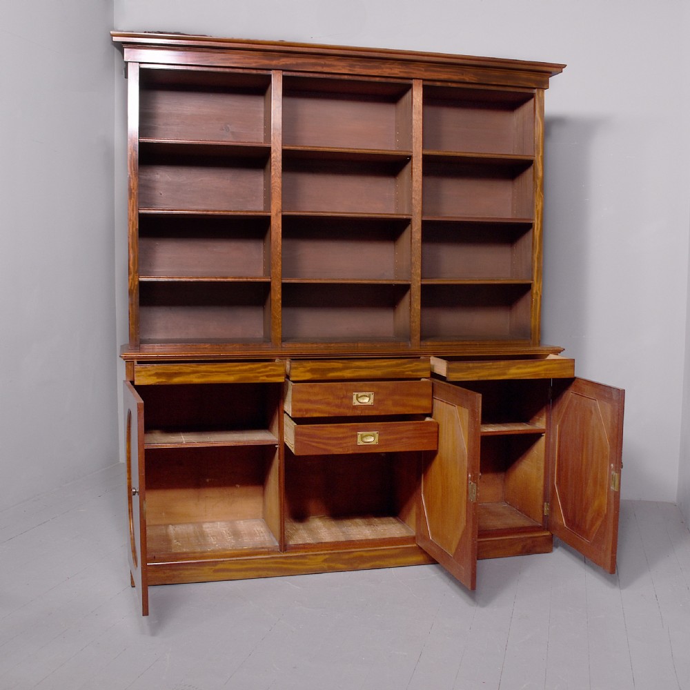 A large mid-Victorian mahogany bookcase featuring a three-bay open upper section with adjustable shelves set above a three-door cupboard base with oval veneered panels. View XIII