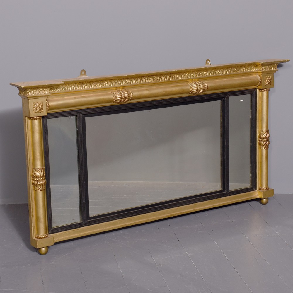 A horizontal Regency giltwood triptych overmantel mirror featuring acanthus leaf columns, a breakfront cornice, and three mirror plates framed with ebonised inner slip.