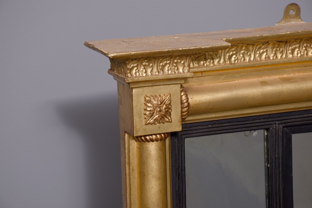 A horizontal Regency giltwood triptych overmantel mirror featuring acanthus leaf columns, a breakfront cornice, and three mirror plates framed with ebonised inner slip. View IV