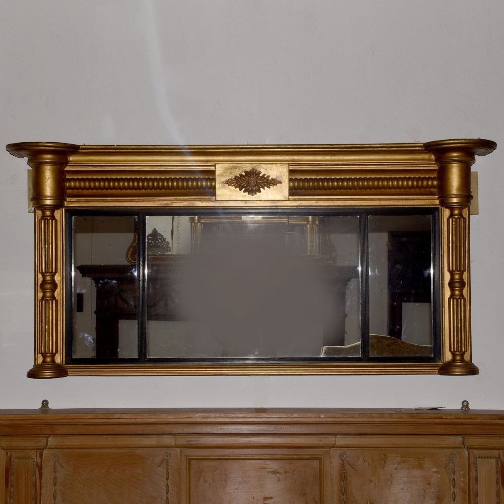 A horizontal Regency giltwood triptych overmantel mirror featuring three mirror plates flanked by fluted columns and topped with a beaded cornice.