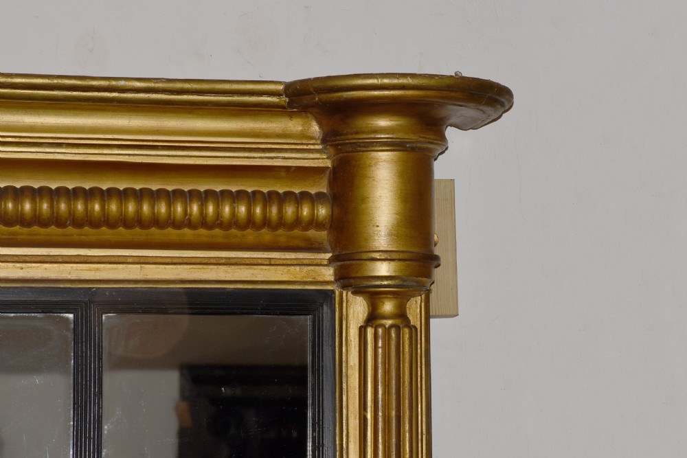 A horizontal Regency giltwood triptych overmantel mirror featuring three mirror plates flanked by fluted columns and topped with a beaded cornice. View IV