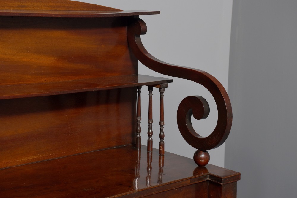 A dark mahogany Regency chiffonier featuring an upper open shelf supported by scrolled sides and two lower cupboard doors with diamond brass grilles. View II