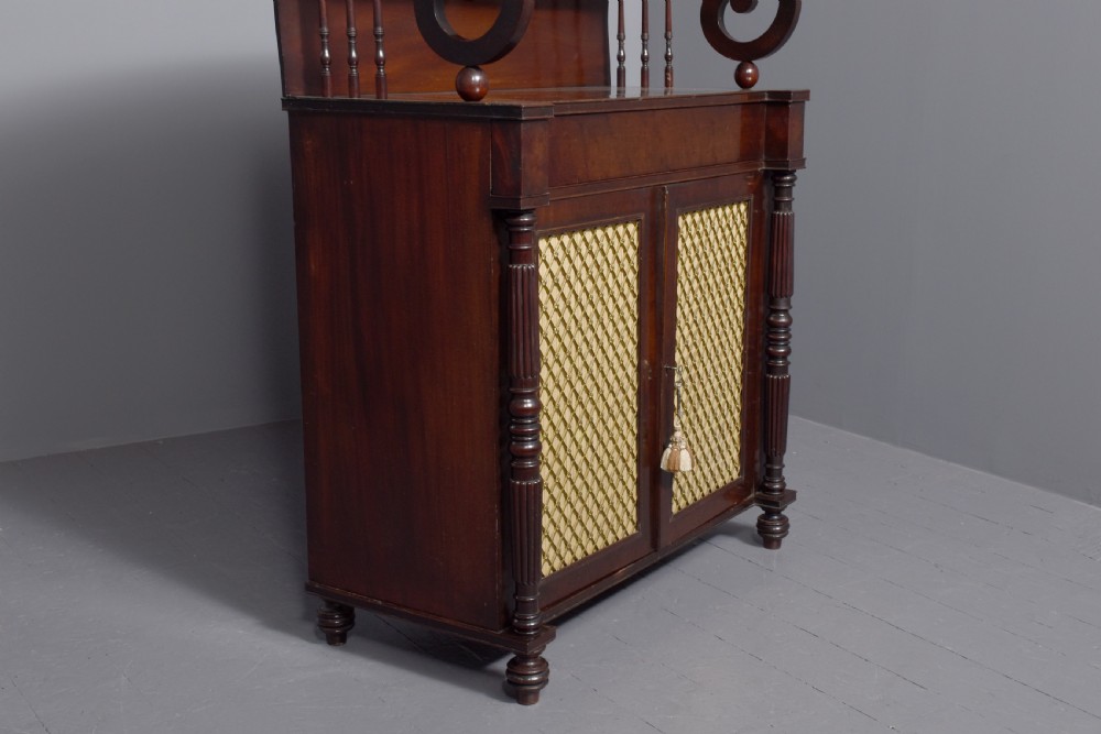 A dark mahogany Regency chiffonier featuring an upper open shelf supported by scrolled sides and two lower cupboard doors with diamond brass grilles. View V