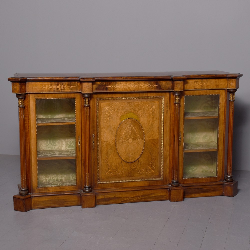 A mid-Victorian burr walnut credenza featuring a central panel door with floral marquetry inlay, flanked by two glazed display doors housing fabric-lined shelves.