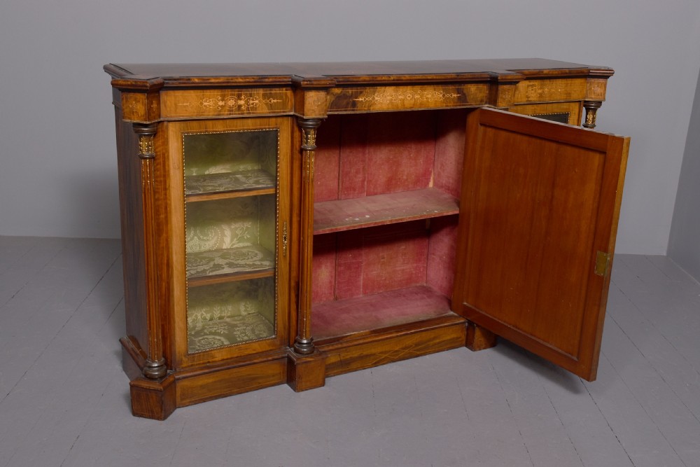 A mid-Victorian burr walnut credenza featuring a central panel door with floral marquetry inlay, flanked by two glazed display doors housing fabric-lined shelves. View VI