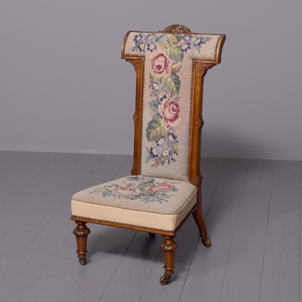 A Victorian prie-dieu chair featuring floral needlepoint upholstery on a carved wood frame with turned front legs and brass castors.