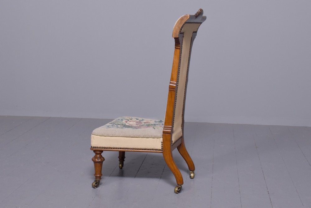 A Victorian prie-dieu chair featuring floral needlepoint upholstery on a carved wood frame with turned front legs and brass castors. View VI