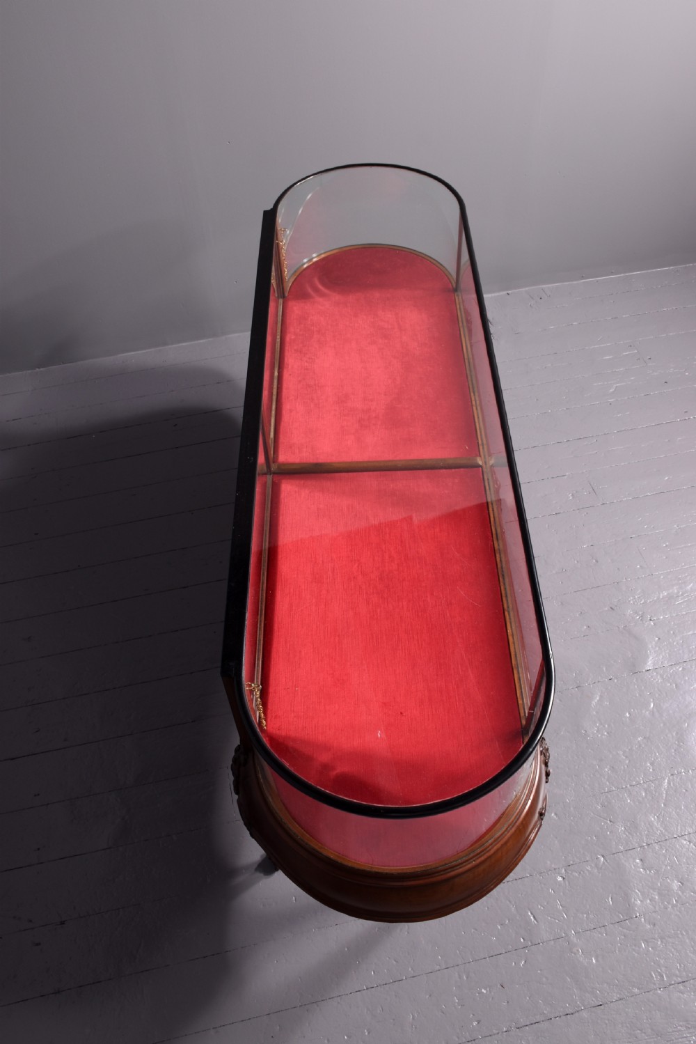 A large oval mahogany display cabinet featuring curved glass sides, red velvet lining, carved cabriole legs, and claw and ball feet. View VI