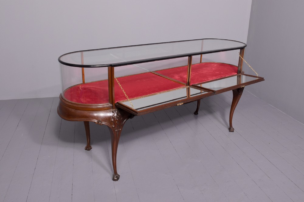 A large oval mahogany display cabinet featuring curved glass sides, red velvet lining, carved cabriole legs, and claw and ball feet. View VIII