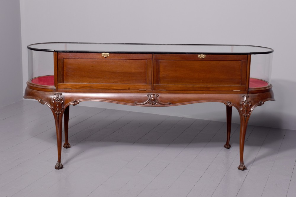 A large oval mahogany display cabinet featuring curved glass sides, red velvet lining, carved cabriole legs, and claw and ball feet. View X