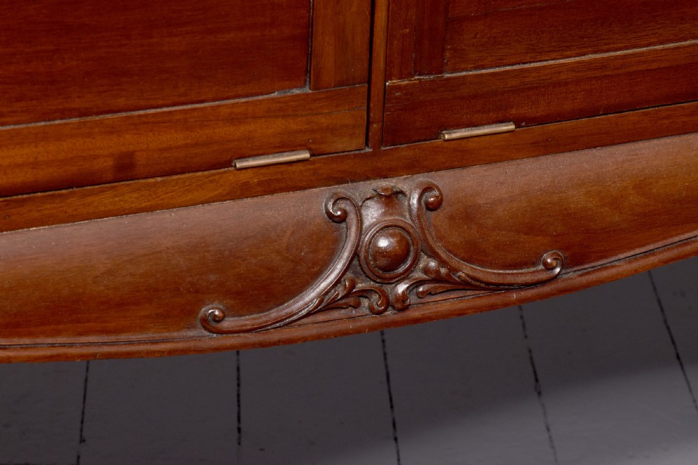 A large oval mahogany display cabinet featuring curved glass sides, red velvet lining, carved cabriole legs, and claw and ball feet. View XII