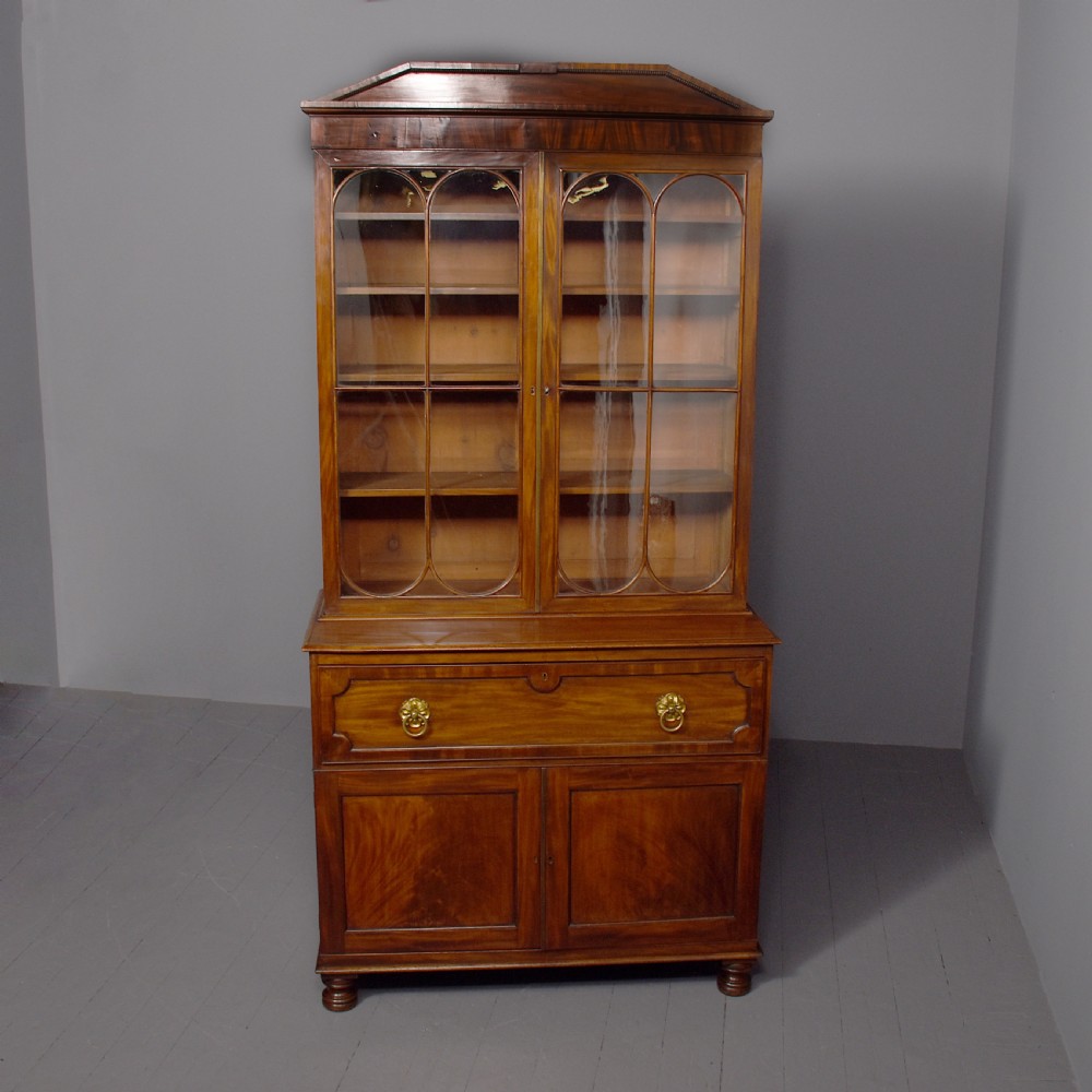 A George IV mahogany secretaire bookcase featuring arched astragal glazed doors, a fitted pull-out writing drawer with brass handles, and twin cupboard doors below.