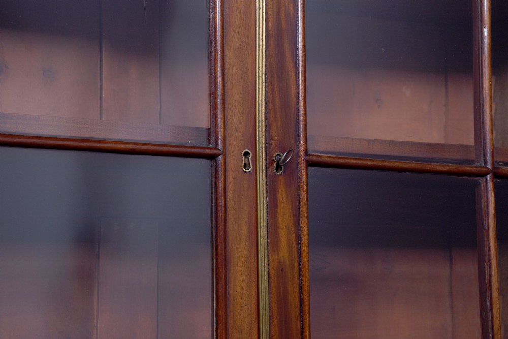 A George IV mahogany secretaire bookcase featuring arched astragal glazed doors, a fitted pull-out writing drawer with brass handles, and twin cupboard doors below. View IV