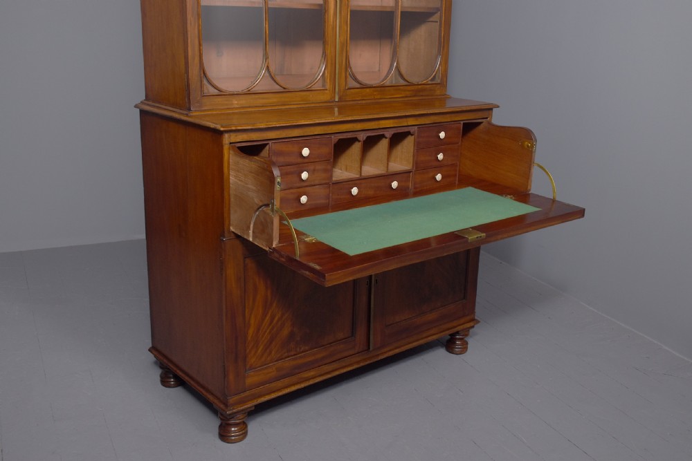 A George IV mahogany secretaire bookcase featuring arched astragal glazed doors, a fitted pull-out writing drawer with brass handles, and twin cupboard doors below. View VII