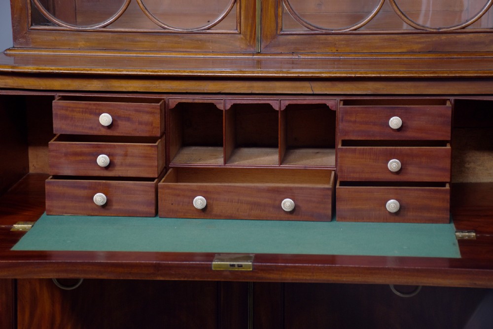 A George IV mahogany secretaire bookcase featuring arched astragal glazed doors, a fitted pull-out writing drawer with brass handles, and twin cupboard doors below. View VIII