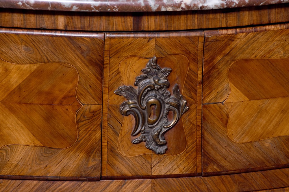 A Louis XV style bombee commode featuring a variegated marble top, geometric timber parquetry, three drawers, and ornate bronze handles. View II