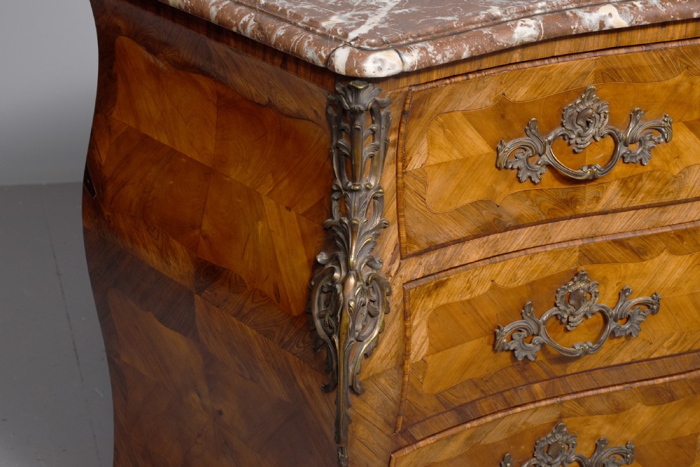 A Louis XV style bombee commode featuring a variegated marble top, geometric timber parquetry, three drawers, and ornate bronze handles. View V