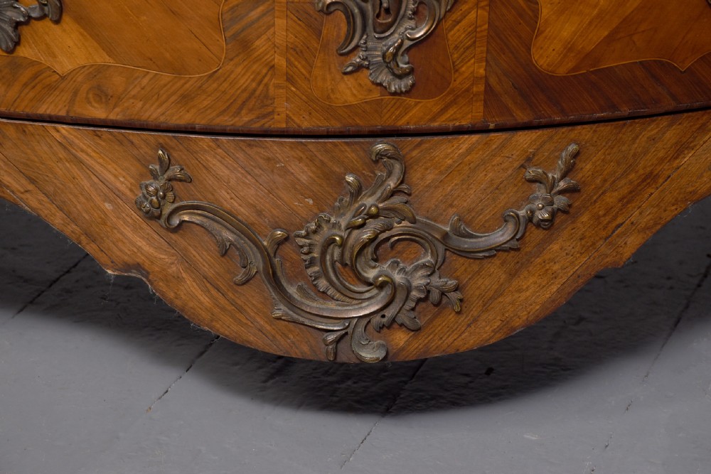 A Louis XV style bombee commode featuring a variegated marble top, geometric timber parquetry, three drawers, and ornate bronze handles. View VI
