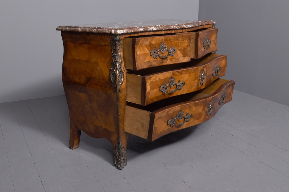 A Louis XV style bombee commode featuring a variegated marble top, geometric timber parquetry, three drawers, and ornate bronze handles. View IX