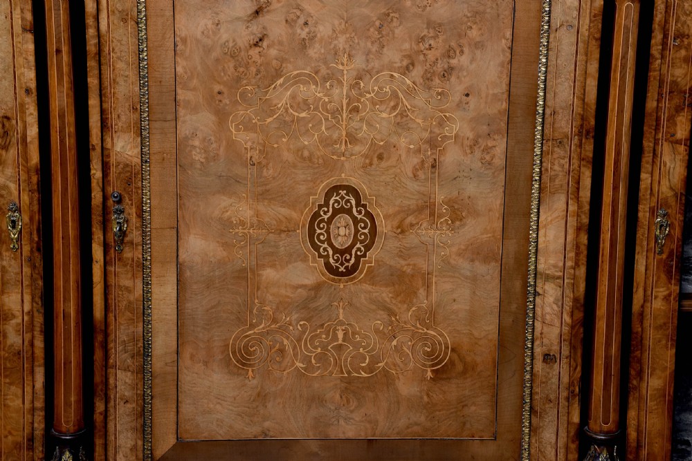 A Victorian burr walnut credenza featuring a central marquetry inlaid panel door flanked by two curved glazed display cupboards and gilt-bronze mounts. View VI