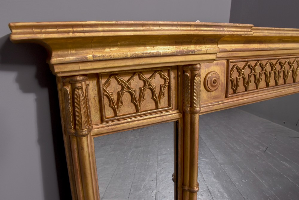 A wide Regency giltwood tryptic overmantel mirror featuring three mirror plates, carved blind tracery frieze, and reeded upright columns. View II