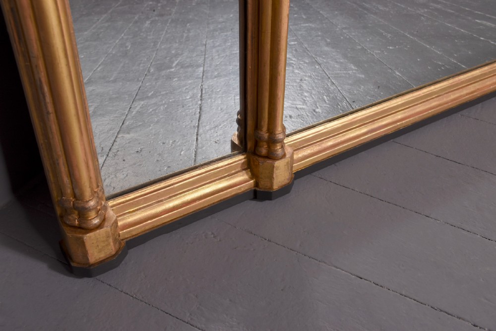 A wide Regency giltwood tryptic overmantel mirror featuring three mirror plates, carved blind tracery frieze, and reeded upright columns. View III