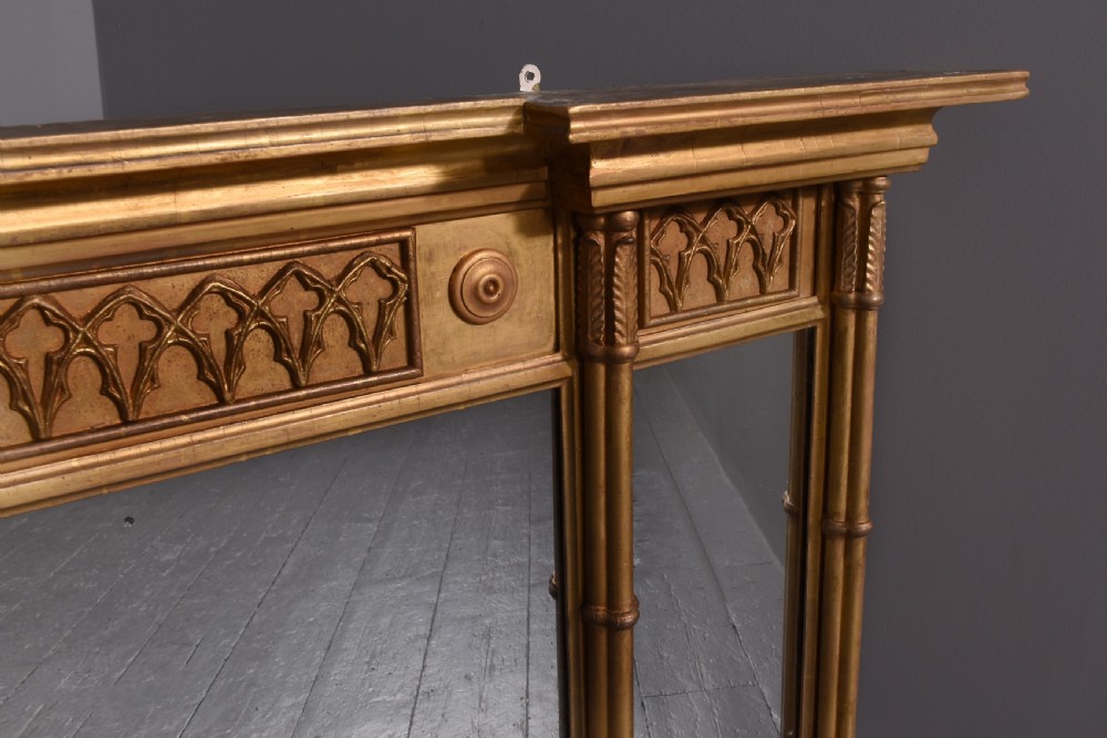 A wide Regency giltwood tryptic overmantel mirror featuring three mirror plates, carved blind tracery frieze, and reeded upright columns. View IV