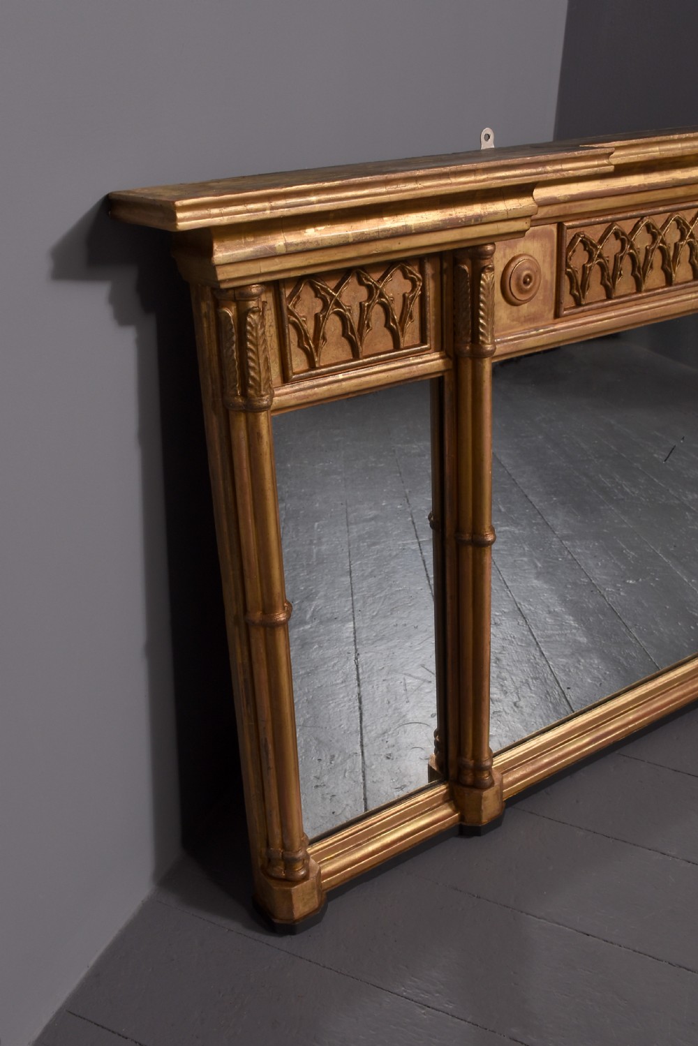 A wide Regency giltwood tryptic overmantel mirror featuring three mirror plates, carved blind tracery frieze, and reeded upright columns. View V