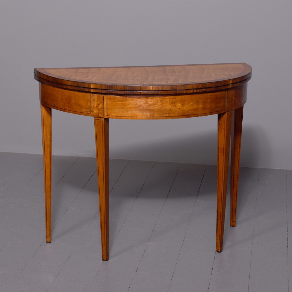 A late 18th-century George III semi-circular satinwood card table featuring crossbanded inlay borders and four square tapered legs.