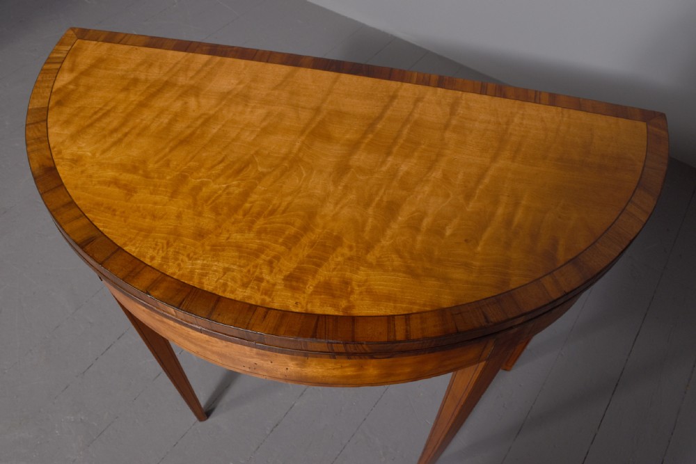 A late 18th-century George III semi-circular satinwood card table featuring crossbanded inlay borders and four square tapered legs. View V