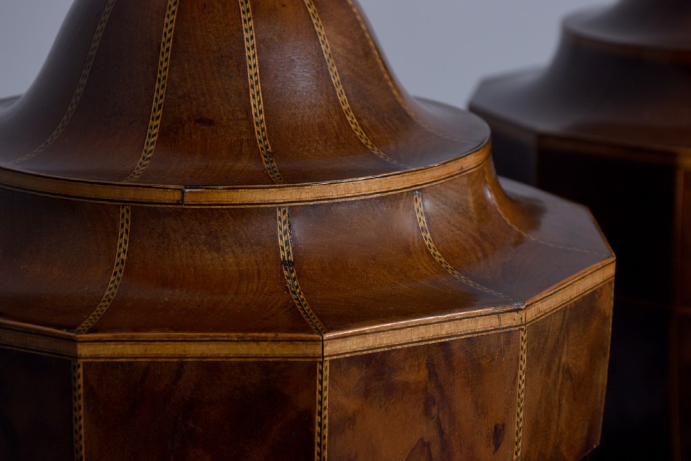 A pair of faceted mahogany cutlery urns featuring geometric stringing inlay, turned finials, and silver keyhole escutcheons on square pedestals. View VII