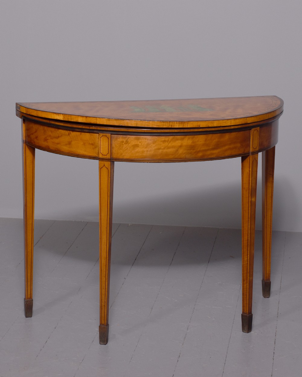 A George III demi-lune satinwood card table with painted decorative motifs, string inlay, and four square tapered legs.