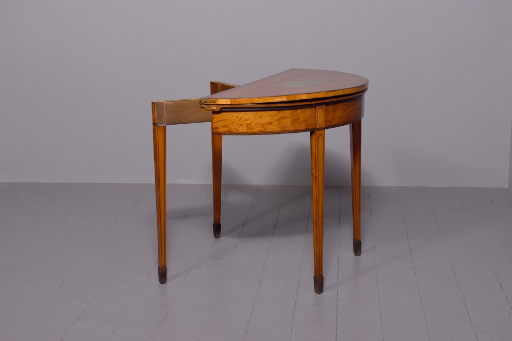 A George III demi-lune satinwood card table with painted decorative motifs, string inlay, and four square tapered legs. View V