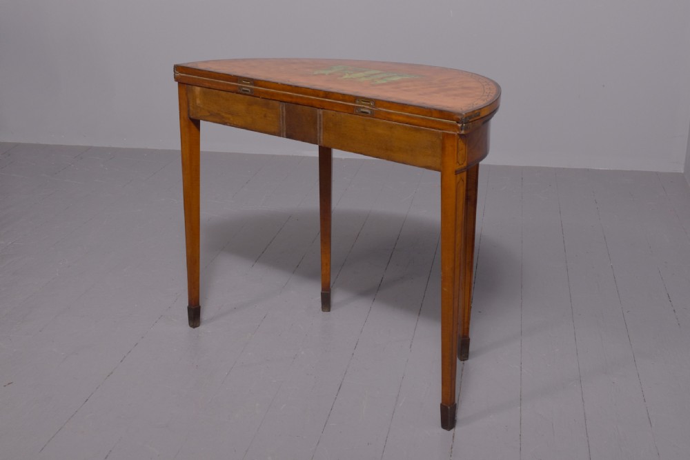A George III demi-lune satinwood card table with painted decorative motifs, string inlay, and four square tapered legs. View VII