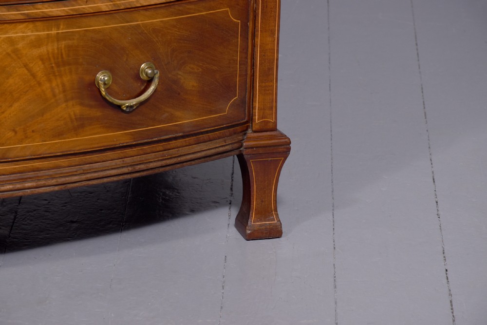 A four-drawer mahogany bow-fronted chest featuring delicate boxwood stringing inlay, brass handles, and splayed bracket feet against a neutral studio backdrop. View II