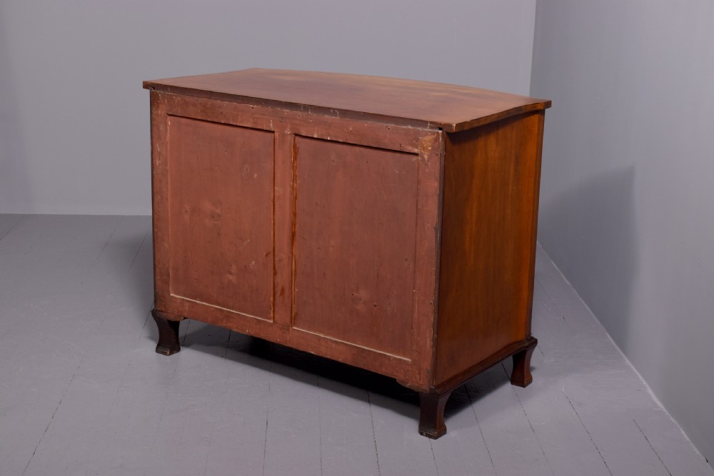 A four-drawer mahogany bow-fronted chest featuring delicate boxwood stringing inlay, brass handles, and splayed bracket feet against a neutral studio backdrop. View VIII